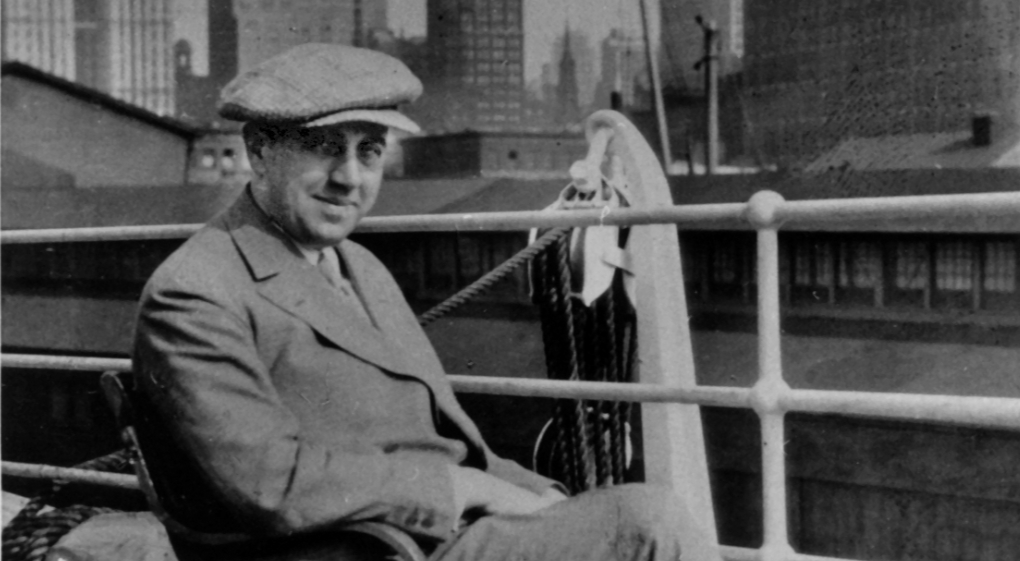 Die Schwarz-Weiß-Aufnahme von 1929 zeigt den damals 39-Jährigen Ernst Reuter. Er sitzt an einer Schiffsreling, trägt eine Schiebermütze und einen Anzug und blickt direkt in die Kamera. Im Hintergrund sind die Umrisse der New Yorker Hochhäuser zu erkennen. Das Foto entstand während einer Studienreise in die USA.